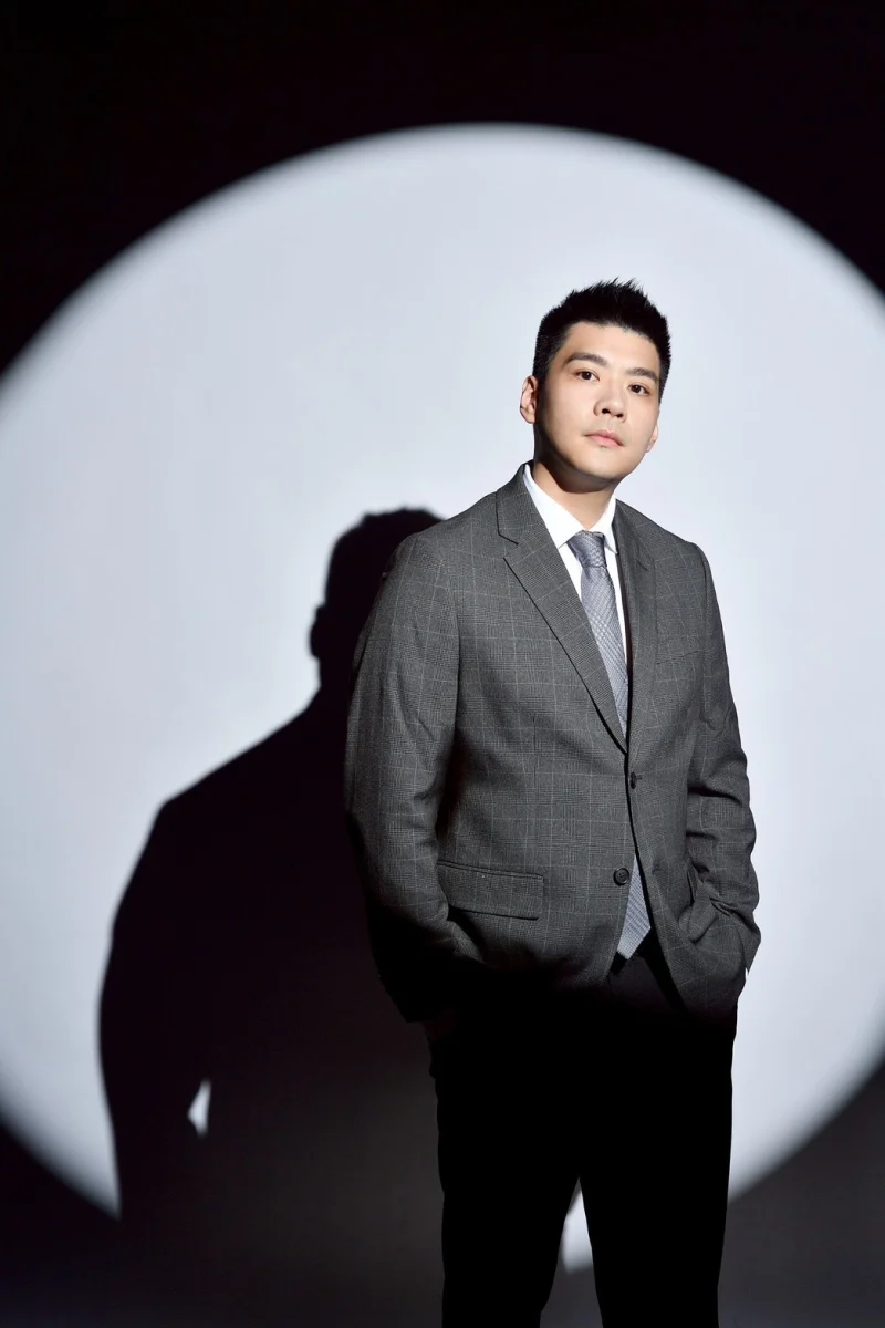 陳仁易會計師穿著灰色格紋西裝，站在聚光燈前